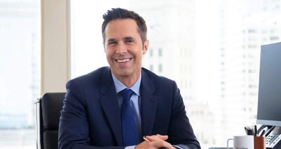 A smiling businessman seated behind a desk.